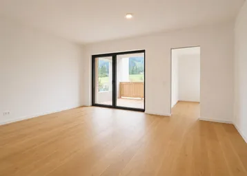 Heller, unmöblierter Wohnraum mit Holzboden und Zugang zu einem Balkon mit Bergblick.