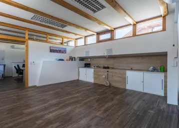 Großzügiger Büroraum mit Holzbalken, großen Fenstern und integrierten Schränken, ideal für kreatives Arbeiten.