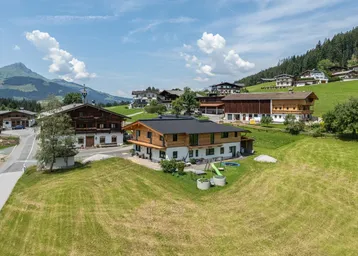 Luftaufnahme eines modernen Hauses in alpiner Umgebung mit grünen Wiesen und Bergblick.