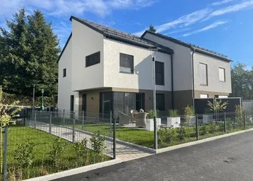 Modernes Reihenhaus mit gepflegtem Vorgarten und kleiner Terrasse unter blauem Himmel.