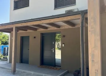 Moderne Hausfassade mit überdachtem Eingangsbereich und Jalousien an den Fenstern.