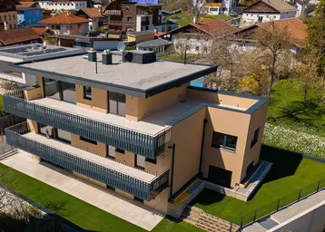 Moderne Wohnanlage mit mehreren Balkonen und Flachdach, umgeben von gepflegtem Rasen und weiteren Häusern.