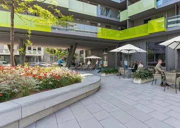 Moderner Innenhof mit Sitzgelegenheiten, Blumenbeeten und Blick auf die farbigen Balkone des Gebäudes.