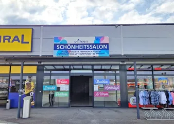 Vorderansicht eines Geschäftshauses mit großem "Schönheitssalon" Schild und weiteren Ladenfronten.