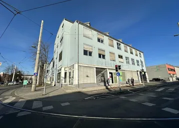 Außenansicht eines Geschäftsgebäudes an einer Straßenecke mit Straßenbahnschienen und blauer Fassade.