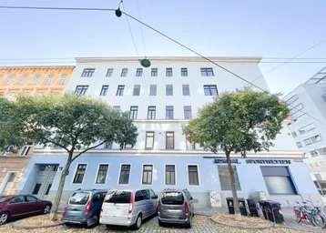 Historisches Mehrfamilienhaus mit blauer Fassade und Parkplätzen davor, in einer städtischen Umgebung.