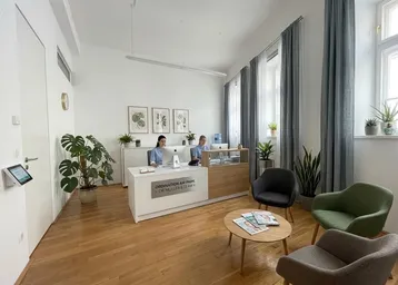 Heller Empfangsbereich mit Holzboden, modernen Möbeln und großen Fenstern, die viel Tageslicht hereinlassen.