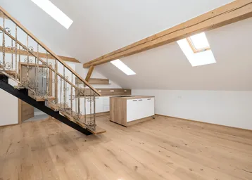 Heller offener Wohnbereich im Dachgeschoss mit moderner Küche, Holzbalken und schmiedeeiserner Treppe.