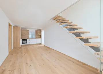 Heller offener Wohnbereich mit moderner Einbauküche, Holzfußboden und eleganter Holztreppe mit Glasgeländer.