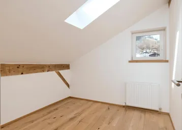 Gemütliches Zimmer im Dachgeschoss mit Holzdielenboden, Dachfenster und Blick auf die umliegende Berglandschaft.