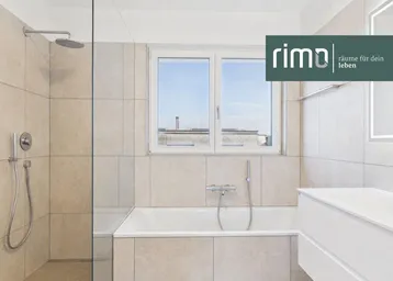 Modernes Badezimmer mit Badewanne, Regendusche und Fenster, hell gefliest und mit Logo.
