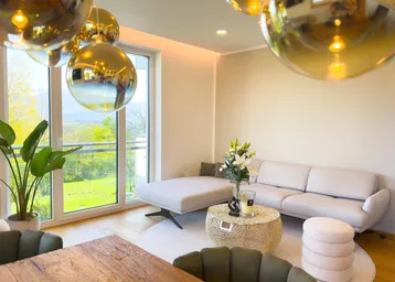 Gemütlicher Wohnbereich mit beigem Sofa, Holzboden und großen Fenstern mit Aussicht.
