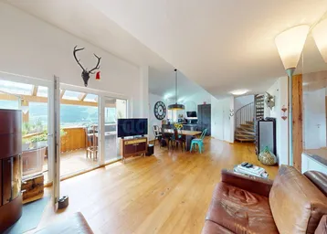 Geräumiger offener Wohn- und Essbereich mit Holzboden, Kaminofen und Zugang zum Balkon mit Bergblick.