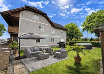 Sonniger Gartenbereich mit gemütlicher Lounge-Ecke, Grill und Whirlpool vor dem traditionellen Haus.