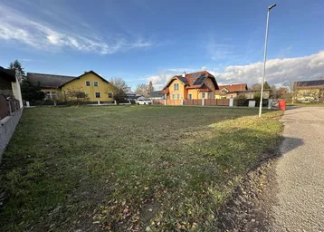 Leeres Grundstück mit angrenzender Straße und umliegenden Wohnhäusern unter blauem Himmel.