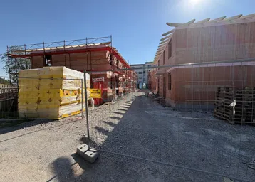 Neubauhäuser im Rohbauzustand an einem sonnigen Tag, umgeben von Bauzäunen und Materialien.
