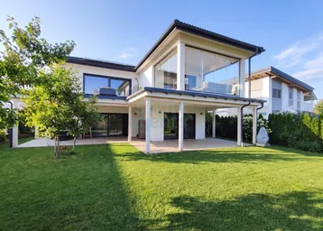 Modernes Einfamilienhaus mit großer Rasenfläche und verglastem Obergeschossbereich.