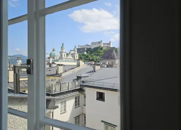 Blick aus dem Fenster auf die historische Stadt Salzburg mit Festung Hohensalzburg und Dächern.