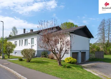 Ansicht des Hauses von vorne mit zwei Garagen und gepflegtem Vorgarten unter blauem Himmel.