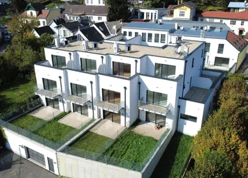 Modernes Wohngebäude mit Flachdach, Balkonen und privaten Gärten in einer grünen Umgebung.