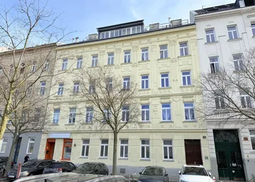 Historisches Gebäude mit gelber Fassade und vielen Fenstern an einer städtischen Straße.