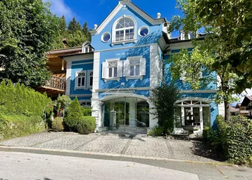 Historisches Gebäude mit leuchtend blauer Fassade, weißen Fensterläden und einem eleganten Eingangsbereich.