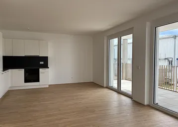 Heller offener Wohnbereich mit integrierter Küche, Parkettboden und Zugang zu einer Terrasse.