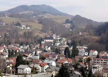 Panoramablick auf ein malerisches Dorf eingebettet in eine hügelige Landschaft mit bewaldeten Bergen im Hintergrund.