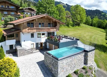 Großzügiges Chalet mit Infinity-Pool und weitläufiger Terrasse, umgeben von grüner Berglandschaft.