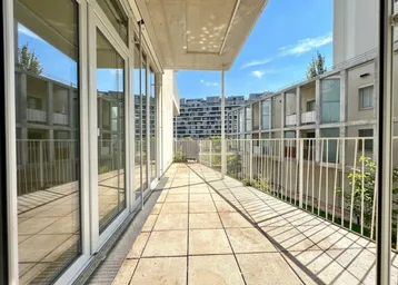 Langer Balkon mit Fliesenboden und weißem Geländer, bietet Blick auf moderne Wohngebäude.