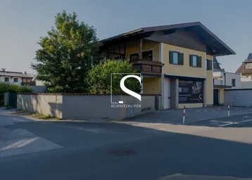 Gebäude mit gelber Fassade, Holzbalkonen und ummauertem Vorgarten an einer Straße.