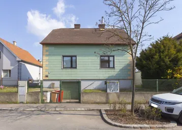Einfaches Einfamilienhaus mit grün-gelber Fassade und Satteldach in ländlicher Umgebung.