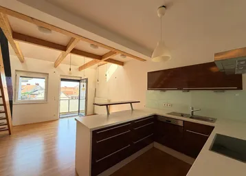 Heller offener Wohnbereich mit integrierter Küche, Holzbalken und Zugang zu einem Balkon.