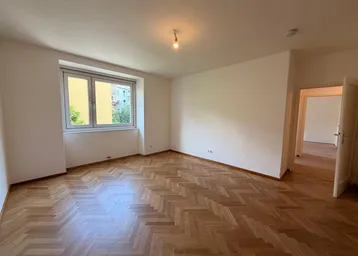 Helles Zimmer mit Fischgrätparkettboden und Blick ins Grüne, bereit zur individuellen Gestaltung.