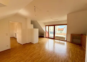 Helles Dachgeschoss-Wohnzimmer mit Parkettboden, Dachschrägen und Zugang zu einer großen Terrasse.