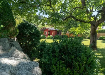 Idyllischer Gartenbereich mit gepflegtem Rasen, Bäumen und einem charmanten roten Gartenhaus im Hintergrund.