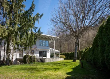 Großzügiger Gartenbereich mit Rasenfläche und hohen Bäumen hinter einem modernen Wohnhaus.