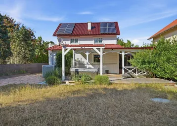 Großer Gartenbereich mit Rasenfläche, Holzterrasse, Whirlpool und einem Haus mit Solaranlage auf dem Dach.