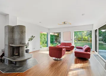 Helles Wohnzimmer mit modernem Kamin, roten Sofas und großen Fenstern zum Garten.