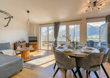 Heller Wohn- und Essbereich mit Holzboden, modernen Möbeln und Zugang zum Balkon mit Bergblick.