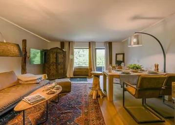 Gemütlicher Wohn-Essbereich mit Holzboden, traditionellem Teppich und Zugang zum Balkon.
