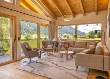 Helles Wohnzimmer mit Holzbalkendecke, großen Fenstern und Bergblick in modernem Design.
