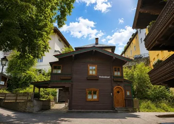 Traditionelles Holzhaus im Chalet-Stil mit dunkler Fassade und grünen Akzenten unter blauem Himmel.