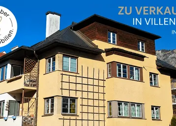 Gelbe Fassade eines Hauses in Villenlage mit Blick auf die Berge und blauen Himmel.