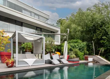 Moderne Villa mit luxuriösem Außenpool, Holzterrasse und stilvollen Lounge-Möbeln, umgeben von üppigem Grün.