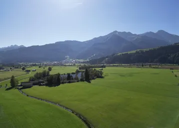 Weitläufige grüne Landschaft mit Bergen, einem See und einem kleinen Dorf in der Ferne.