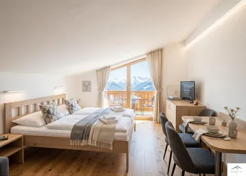 Helles Schlafzimmer mit Holzboden, Bergblick und Zugang zu einem Balkon, inklusive Essbereich.