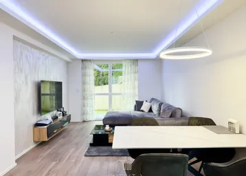 Lichtdurchfluteter Wohn-Essbereich mit Zugang zum Garten, modernem Sofa und dekorativer Wandgestaltung.