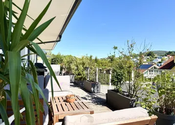 Sonnige Terrasse mit bequemen Gartenmöbeln, vielen Pflanzen und weitem Blick über die grüne Umgebung.