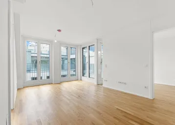 Helles Wohnzimmer mit großen Fenstern, Holzboden und Zugang zu einem französischen Balkon.